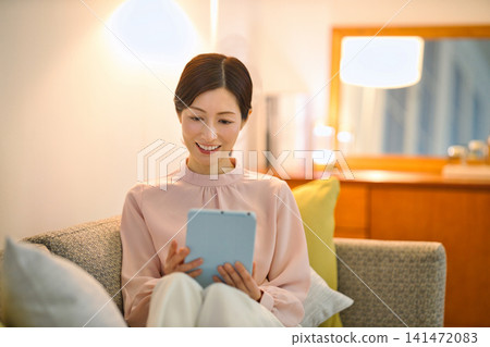 一位四十多歲的女性晚上在房間裡放鬆地看著平板電腦。 一位四十多歲的女性晚上在房間裡放鬆地看著平板電腦。 141472083