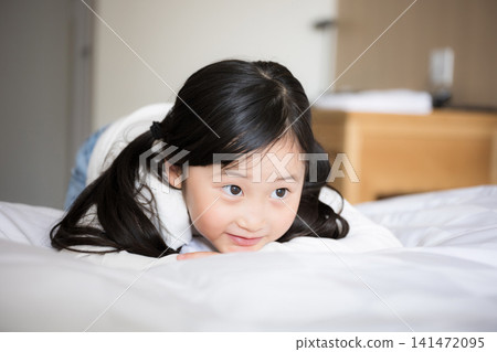 A smiling Japanese girl relaxing on a hotel bed. An image of a family trip or hotel stay. A smiling Japanese girl relaxing on a hotel bed. An image of a family trip or hotel stay. 141472095