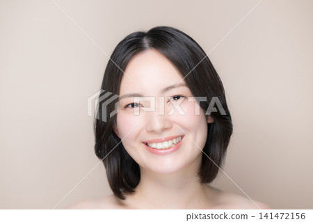 A beautiful Japanese woman with a pinkish-beige background, showcasing her flawless skin and natural makeup, is featured in a close-up shot of her smiling and looking directly at the camera. A beautiful Japanese woman with a pinkish-beige background, showcasing her flawless skin and natural makeup, is featured in a close-up shot of her smiling and looking directly at the camera. 141472156