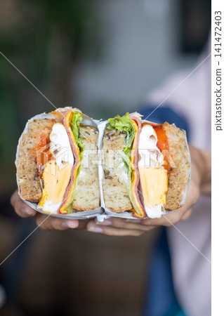 Fresh Whole Wheat Sandwich with Ham Cheese Egg Lettuce and Tomato Held in Hands, Healthy Breakfast, Homemade Lunch, Takeaway Cafe Food, Close Up Lifestyle Food Photography Fresh Whole Wheat Sandwich with Ham Cheese Egg Lettuce and Tomato Held in Hands, Healthy Breakfast, Homemade Lunch, Takeaway Cafe Food, Close Up Lifestyle Food Photography 141472403
