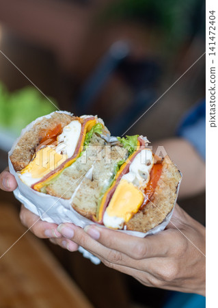 Fresh Whole Wheat Sandwich with Ham Cheese Egg Lettuce and Tomato Held in Hands, Healthy Breakfast, Homemade Lunch, Takeaway Cafe Food, Close Up Lifestyle Food Photography Fresh Whole Wheat Sandwich with Ham Cheese Egg Lettuce and Tomato Held in Hands, Healthy Breakfast, Homemade Lunch, Takeaway Cafe Food, Close Up Lifestyle Food Photography 141472404