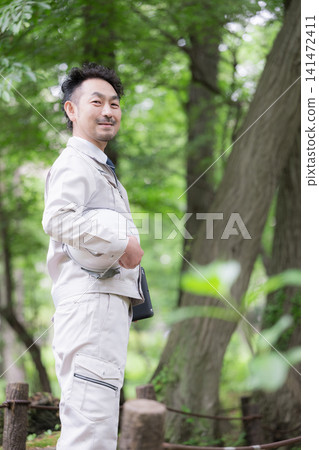 在一片翠綠的環境中,可以看到參與城市規劃基礎設施、林業和建築管理的現場工作人員,他們頭戴頭盔,手持平板電腦,直視鏡頭。 在一片翠綠的環境中,可以看到參與城市規劃基礎設施、林業和建築管理的現場工作人員,他們頭戴頭盔,手持平板電腦,直視鏡頭。 141472411