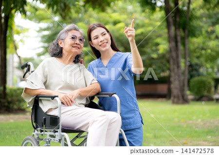 Caucasian female caregiver encouraging senior patient on wheelchair in garden. Caucasian female caregiver encouraging senior patient on wheelchair in garden. 141472578