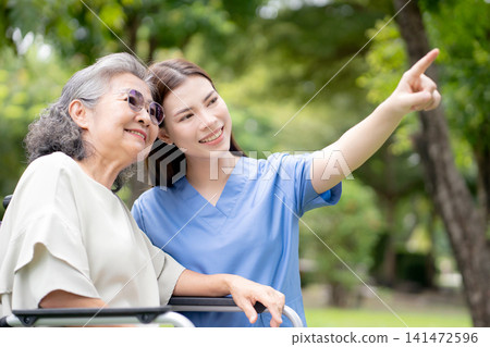 Caucasian female caregiver encouraging senior patient on wheelchair in garden. Caucasian female caregiver encouraging senior patient on wheelchair in garden. 141472596