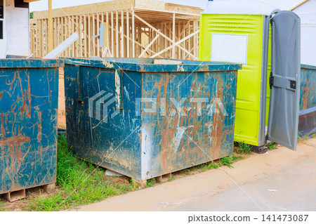 Trash bins sit on ground next to portable toilet at construction site Trash bins sit on ground next to portable toilet at construction site 141473087