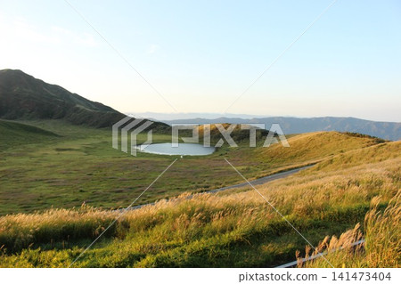 A scene of the sunrise over Kusasenrigahama in Aso City, Kumamoto Prefecture, featuring a vast grassland and pond bathed in the morning sun, and Mount Aso Nakadake with its rising plume of smoke. A scene of the sunrise over Kusasenrigahama in Aso City, Kumamoto Prefecture, featuring a vast grassland and pond bathed in the morning sun, and Mount Aso Nakadake with its rising plume of smoke. 141473404
