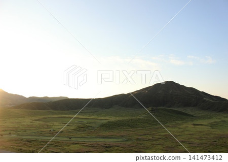 A scene of the sunrise over Kusasenrigahama in Aso City, Kumamoto Prefecture, featuring a vast grassland and pond bathed in the morning sun, and Mount Aso Nakadake with its rising plume of smoke. A scene of the sunrise over Kusasenrigahama in Aso City, Kumamoto Prefecture, featuring a vast grassland and pond bathed in the morning sun, and Mount Aso Nakadake with its rising plume of smoke. 141473412