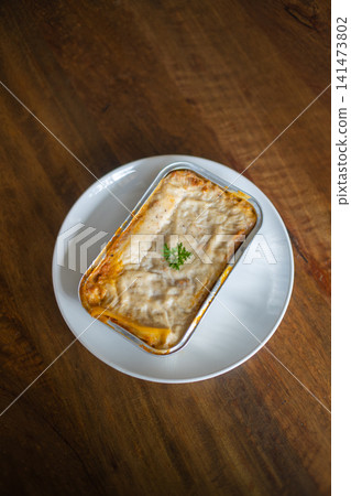 Fresh baked lasagna or macaroni and cheese in aluminum baking tray on white plate, creamy melted cheese comfort food served on rustic wooden table with copy space Fresh baked lasagna or macaroni and cheese in aluminum baking tray on white plate, creamy melted cheese comfort food served on rustic wooden table with copy space 141473802