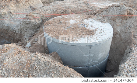 Concrete drainage pipe or manhole component set in a trench. Surrounded by dirt and gravel at a construction site during daylight. Construction of new house of Thailand. 141474304