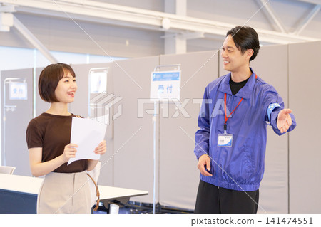 一名工作人員微笑著引導一位女訪客參觀活動場地。 一名工作人員微笑著引導一位女訪客參觀活動場地。 141474551