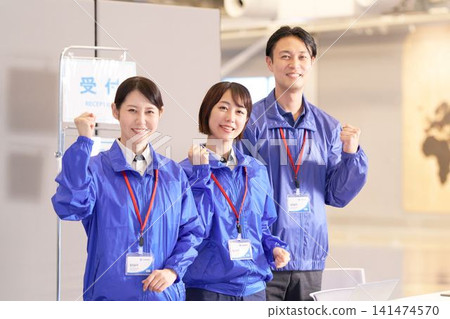 三名男女工作人員在活動場地的接待區前擺出勝利的姿勢。 三名男女工作人員在活動場地的接待區前擺出勝利的姿勢。 141474570