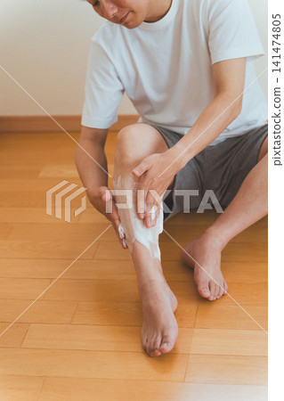 一名四十多歲的男子坐在地板上,往小腿上塗抹刮鬍泡。 一名四十多歲的男子坐在地板上,往小腿上塗抹刮鬍泡。 141474805