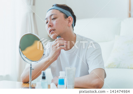 一位四十多歲的男子在桌面鏡子前用電動刮鬍刀刮鬍子。 141474984