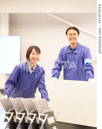 Two staff members, a man and a woman, smiling at the event venue. Two staff members, a man and a woman, smiling at the event venue. 141475014