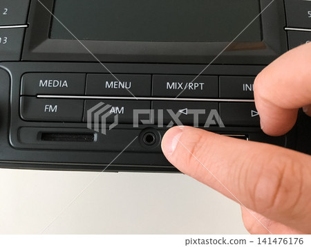 Finger pressing a button on a car radio faceplate with media menu and FM AM controls. Finger pressing a button on a car radio faceplate with media menu and FM AM controls. 141476176