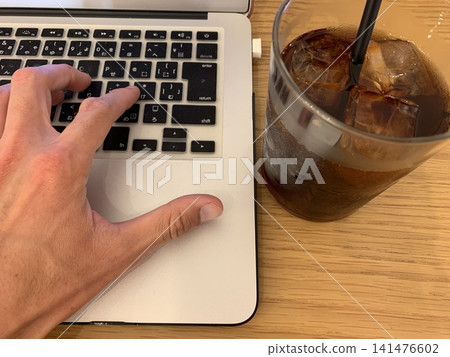 我在咖啡館裡用筆記型電腦工作，手裡拿著一杯冰咖啡。 141476602