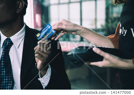 Businessman handing a credit card to cashier holding a payment terminal, showing retail purchase, finance, transaction, banking, commerce, checkout, and cashless payment Businessman handing a credit card to cashier holding a payment terminal, showing retail purchase, finance, transaction, banking, commerce, checkout, and cashless payment 141477000