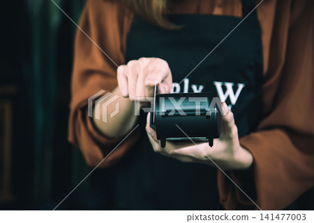 Cashier holding a portable receipt printer and pulling paper after payment, showing checkout, transaction, retail, business, service, finance, commerce, and customer purchase Cashier holding a portable receipt printer and pulling paper after payment, showing checkout, transaction, retail, business, service, finance, commerce, and customer purchase 141477003