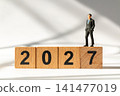 Miniature Businessman Standing on Wooden 2027 Blocks Symbolizing Success and New Year Goals 141477019