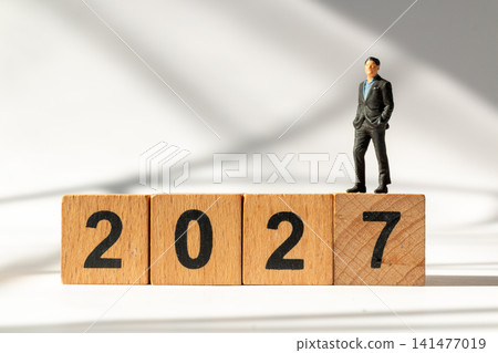 Miniature Businessman Standing on Wooden 2027 Blocks Symbolizing Success and New Year Goals Miniature Businessman Standing on Wooden 2027 Blocks Symbolizing Success and New Year Goals 141477019