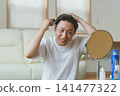 一位四十多歲的男子正在使用電動梳子進行頭皮護理。 141477322