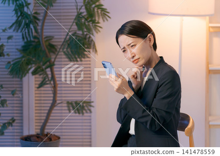 一位身穿西裝的女士看著她的智慧型手機,神情憂慮。 一位身穿西裝的女士看著她的智慧型手機,神情憂慮。 141478559
