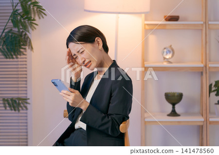 一位身穿西裝的女士看著她的智慧型手機,神情憂慮。 一位身穿西裝的女士看著她的智慧型手機,神情憂慮。 141478560