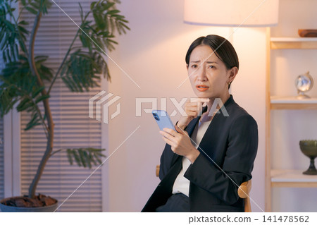 A woman in a suit looking at her smartphone and worrying A woman in a suit looking at her smartphone and worrying 141478562