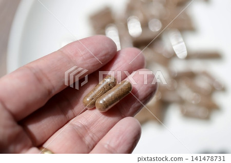 這位女士用指尖夾著兩片米糠補充劑藥片;米糠粉被裝在透明膠囊裡。 這位女士用指尖夾著兩片米糠補充劑藥片;米糠粉被裝在透明膠囊裡。 141478731