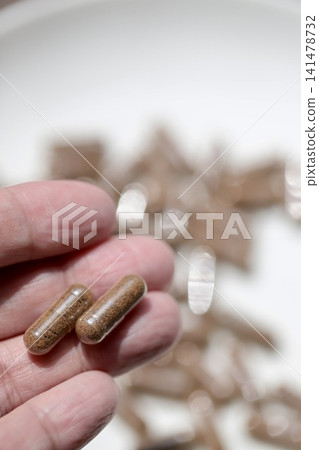 The woman held two rice bran supplement tablets between her fingertips; rice bran powder packed into transparent capsules. The woman held two rice bran supplement tablets between her fingertips; rice bran powder packed into transparent capsules. 141478732