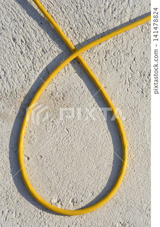 Yellow electric cable loop on textured plaster wall background Yellow electric cable loop on textured plaster wall background 141478824