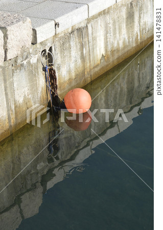 Orange mooring buoy floating by concrete stone dock wall Orange mooring buoy floating by concrete stone dock wall 141478831