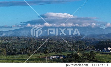 Scenic aerial view of mountain range partially covered by fluffy white clouds under bright blue sky Scenic aerial view of mountain range partially covered by fluffy white clouds under bright blue sky 141479991