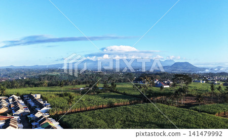 Scenic aerial view of mountain range partially covered by fluffy white clouds under bright blue sky Scenic aerial view of mountain range partially covered by fluffy white clouds under bright blue sky 141479992