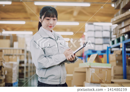 一名穿著工作服的女士在倉庫管理庫存 一名穿著工作服的女士在倉庫管理庫存 141480239