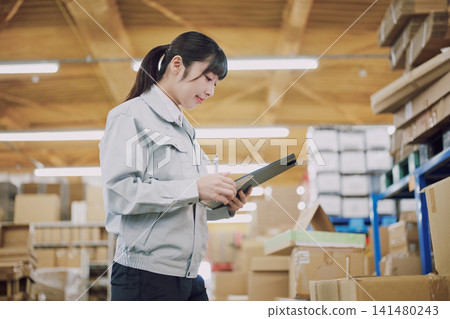 A woman in work clothes managing inventory in a warehouse A woman in work clothes managing inventory in a warehouse 141480243