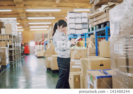 A woman in work clothes managing inventory in a warehouse A woman in work clothes managing inventory in a warehouse 141480244