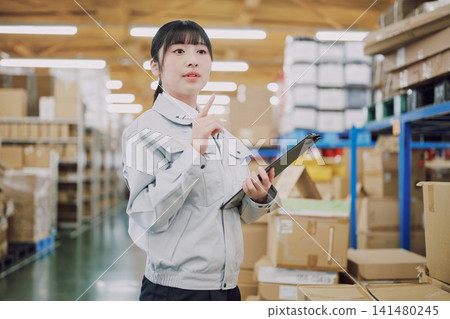 一名穿著工作服的女士在倉庫管理庫存 一名穿著工作服的女士在倉庫管理庫存 141480245