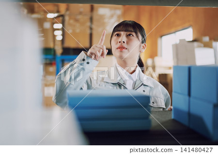 一名穿著工作服的女士在倉庫管理庫存 一名穿著工作服的女士在倉庫管理庫存 141480427