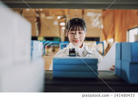 一名穿著工作服的女士在倉庫管理庫存 一名穿著工作服的女士在倉庫管理庫存 141480433