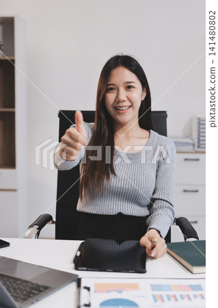 young woman is working on laptop in modern office environment, showcasing focused and productive atmosphere. She is dressed in professional white shirt, with coffee cup and small plant on table, young woman is working on laptop in modern office environment, showcasing focused and productive atmosphere. She is dressed in professional white shirt, with coffee cup and small plant on table, 141480802