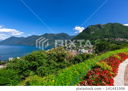 從瑞士盧加諾的花園中眺望湖泊、城鎮和山脈,紅花點綴著綠色的山丘。 從瑞士盧加諾的花園中眺望湖泊、城鎮和山脈,紅花點綴著綠色的山丘。 141481006