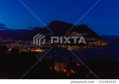 瑞士盧加諾的夜景全景,城市燈光環繞著湖泊,遠處山脈勾勒出迷人的輪廓。 瑞士盧加諾的夜景全景,城市燈光環繞著湖泊,遠處山脈勾勒出迷人的輪廓。 141481010