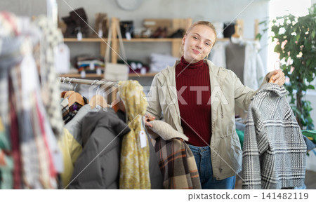 Positive teen girl choosing winter coat in clothing store Positive teen girl choosing winter coat in clothing store 141482119