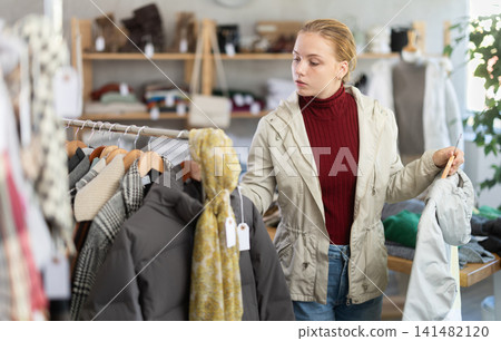 Attentive teenage girl choosing lightweight jacket in clothing store Attentive teenage girl choosing lightweight jacket in clothing store 141482120