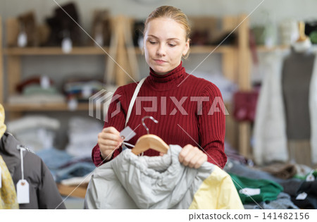 While shopping, teen girl browsing goods items and choose elect down jacket in store 141482156