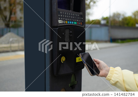 Close up of hand making contactless smartphone payment at city parking meter. Close up of hand making contactless smartphone payment at city parking meter. 141482784