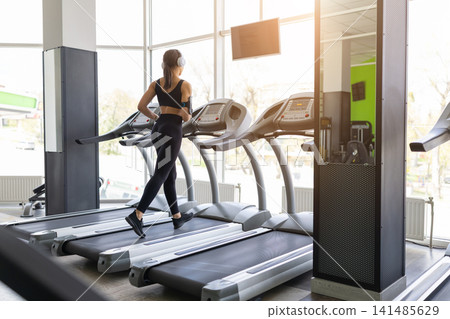 Young Black woman wearing headphones while running on treadmill at gym Young Black woman wearing headphones while running on treadmill at gym 141485629