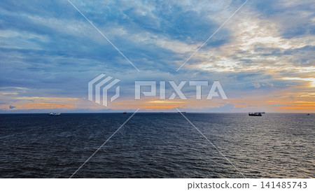 Wide angle view of commercial cargo ships floating on sea horizon under colorful sunset sky for global maritime logistics shipping and travel background Wide angle view of commercial cargo ships floating on sea horizon under colorful sunset sky for global maritime logistics shipping and travel background 141485743