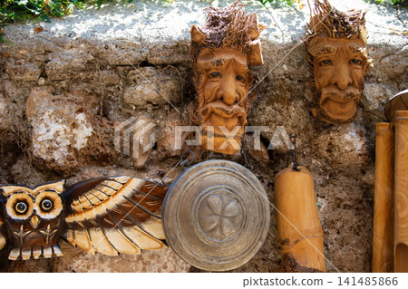 Wooden masks and carvings displayed on a rustic stone wall in a vibrant artisan market during the afternoon sunlight Wooden masks and carvings displayed on a rustic stone wall in a vibrant artisan market during the afternoon sunlight 141485866